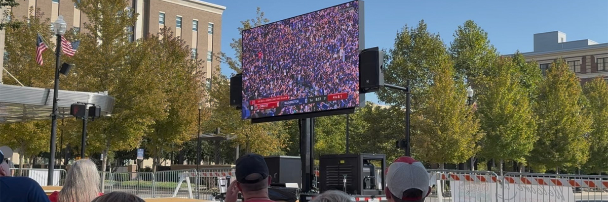 A mobile outdoor trailer LED display screen broadcasting a live World Cup football match to an outdoor crowd in a public square